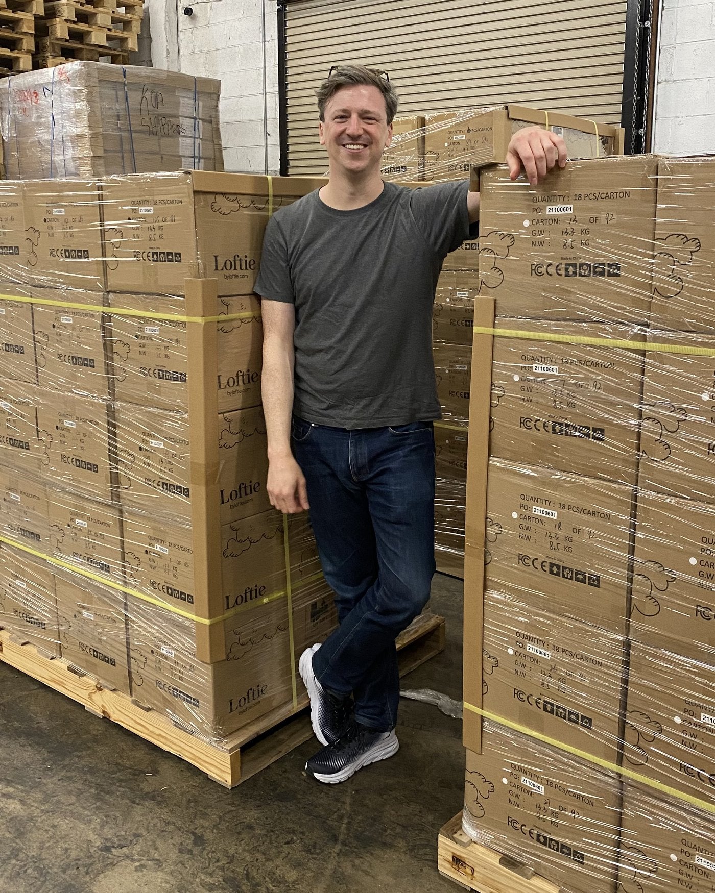 Matthew Hassett, founder and CEO of Loftie, leaning on pallets of boxed Loftie clocks in a warehouse.